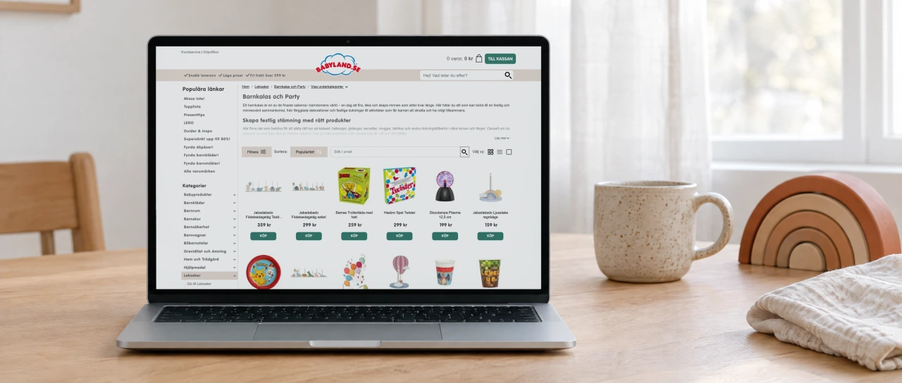Babyland's Barnkalas och Party category page, with its intro and a grid of party products, open on a laptop on an oak dining table in soft daylight.