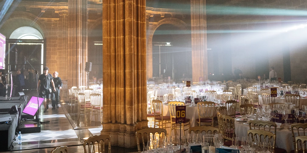 The hall at La Llotja de Mar laid for the gala: stone columns and arches, beams of stage light and round tables set with glasses.