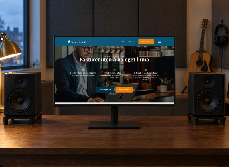 Frilans Finans' Norwegian home page “Fakturer uten å ha eget firma” on a monitor between two studio speakers on an oak desk in a small music room at dusk, with acoustic panels, a guitar and headphones behind.