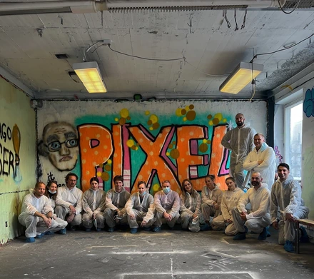 The Pixel Nordic team in white overalls in front of a graffiti wall reading Pixel