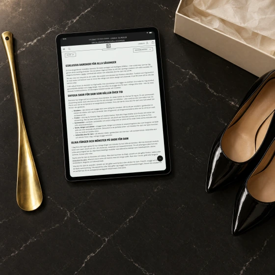 The written text at the foot of NK's page for women's shoes, three headings with paragraphs and a list, on a tablet lying on black marble beside black patent pumps and a brass shoe horn.