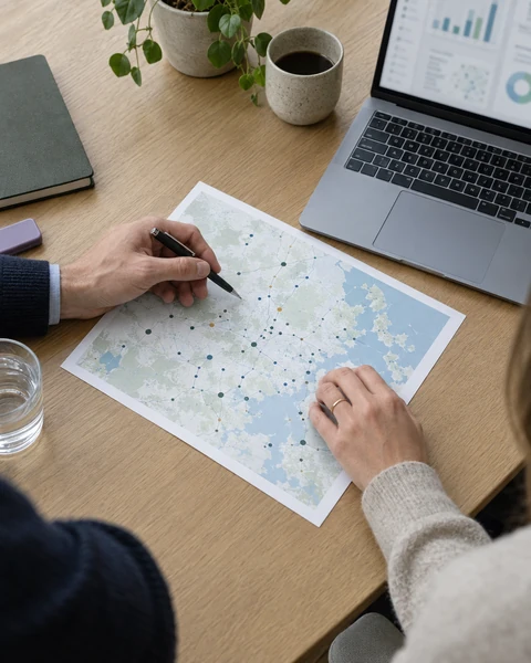 Hands marking a printed map beside a laptop