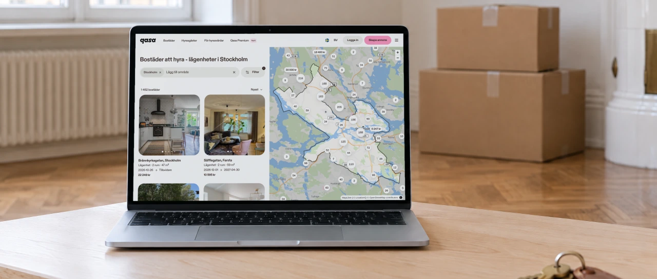 Qasa's page of apartments to rent in Stockholm, with a map of listings and two apartment cards, open on a laptop on a birch coffee table in an empty, freshly painted flat with moving boxes and a set of keys.