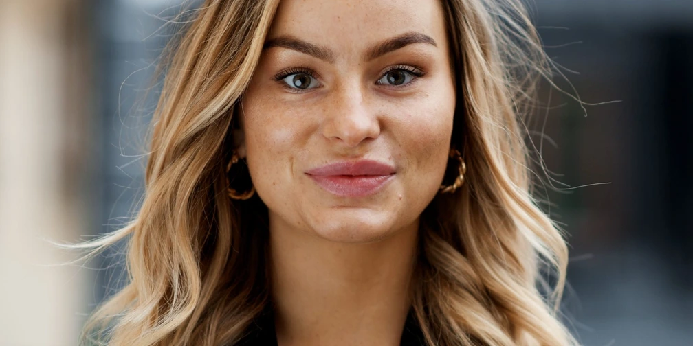 Portrait of Stella Wannberg outdoors, with long wavy hair, gold hoop earrings and a black blouse.