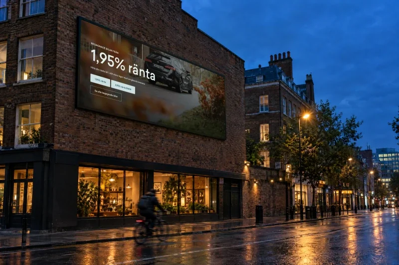 The Holmgrens Bil homepage on a digital billboard on a brick building over a street at dusk