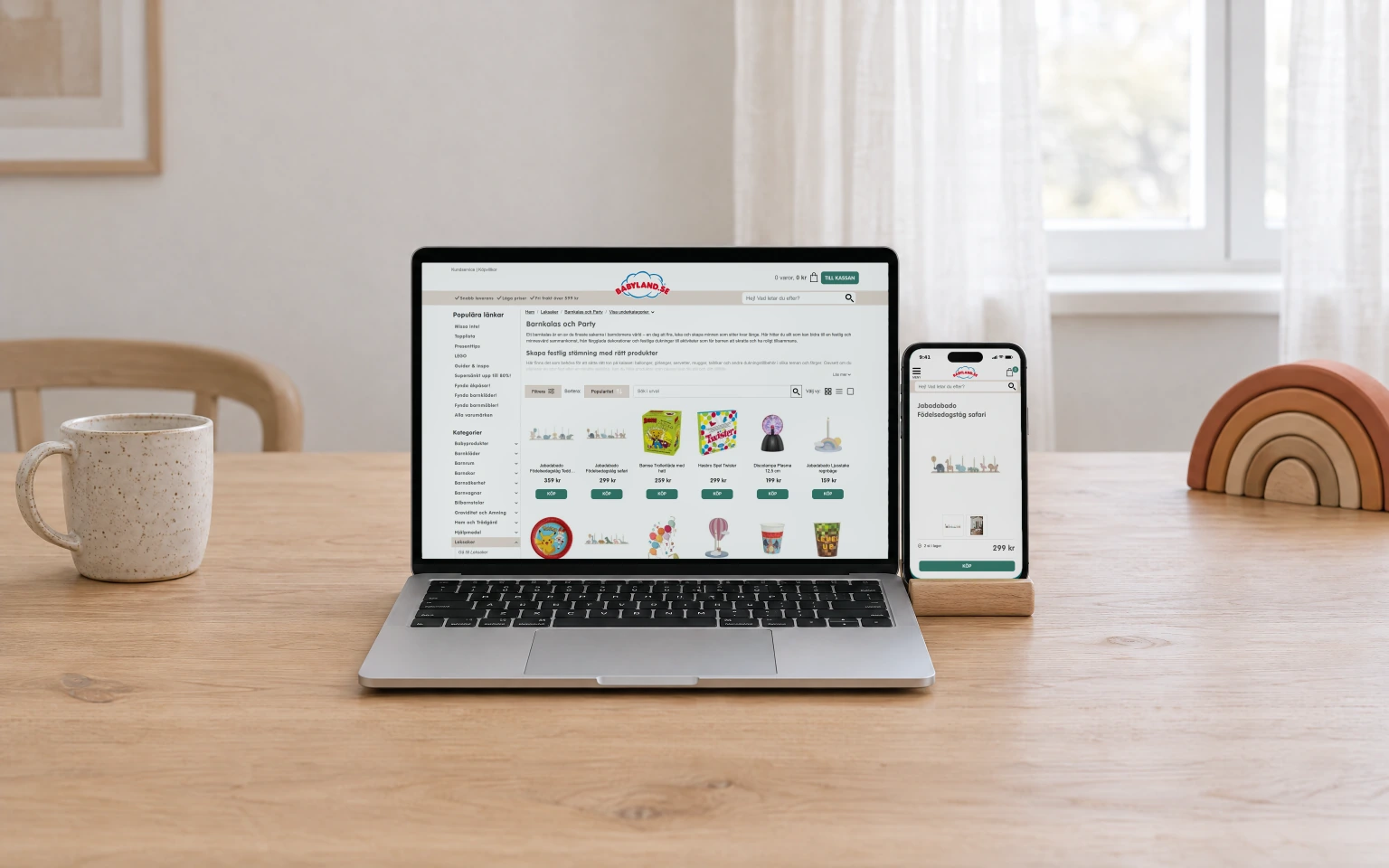 Babyland's Barnkalas och Party page on a laptop, with the product page for a wooden safari birthday train on a phone in a stand beside it.
