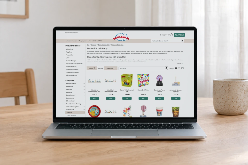 Babyland's Barnkalas och Party category page, with its intro and a grid of party products, open on a laptop on an oak dining table in soft daylight.