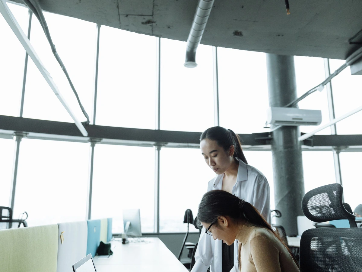 An open-plan office with people working at desks under large windows