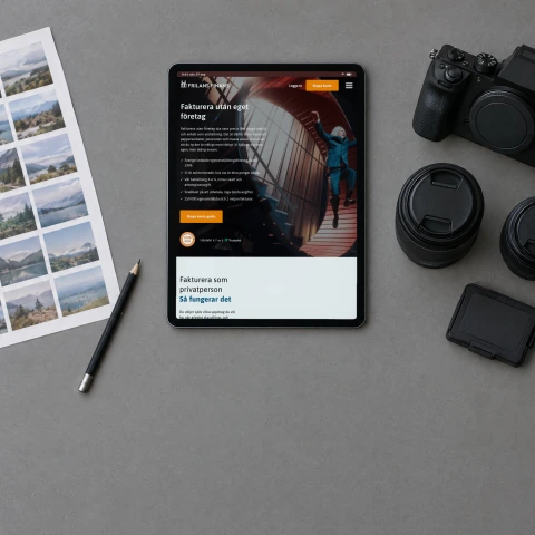Frilans Finans' Swedish home page “Fakturera utan eget företag” (invoicing without your own company) on a tablet lying on a grey work table in a photographer's studio, beside a camera, two lenses and a printed contact sheet
