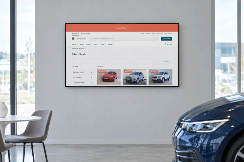Holmgrens Bil's page Bilar till salu, cars for sale with filters and the first three cars, on a large screen on the wall of a car showroom, with the front of a dark blue car in the corner