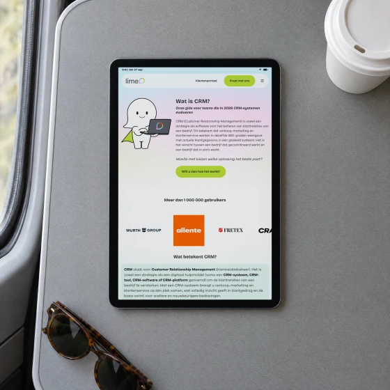 Lime's Dutch guide “Wat is CRM?” on a tablet lying on the fold-down table of a train, beside a paper coffee cup and a pair of sunglasses.