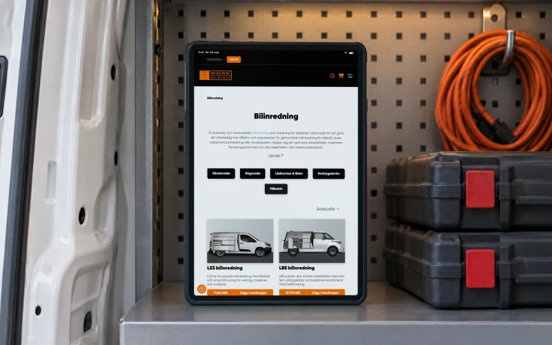 Work System's category page “Bilinredning”, with its introduction, subcategories and the first two racking systems, on a tablet standing on a steel shelf inside a fitted van, beside two tool cases and a coiled orange cable.
