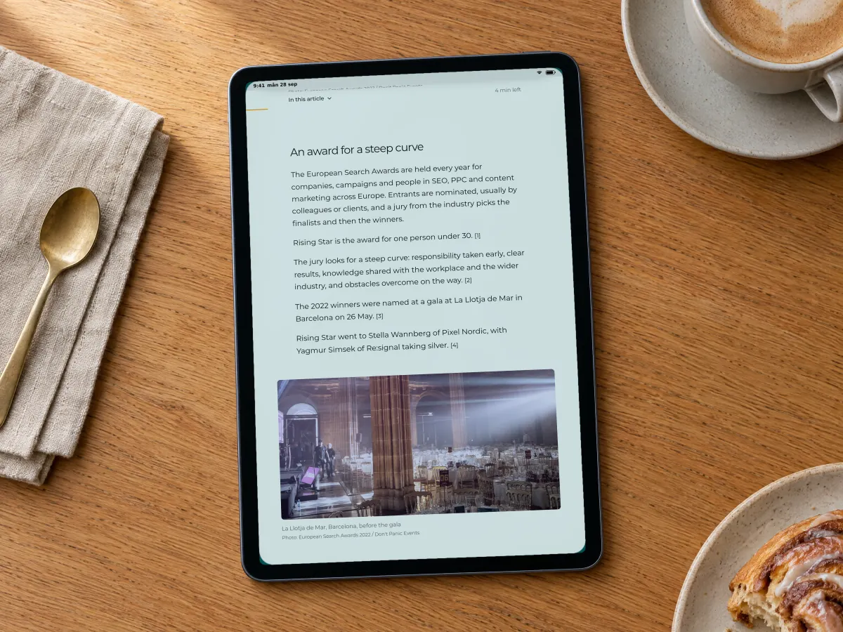 An article on Pixel Nordic's blog about the European Search Awards Rising Star award, with the section An award for a steep curve and a photo of the gala venue, on a tablet on an oak café table beside a flat white and a cinnamon bun