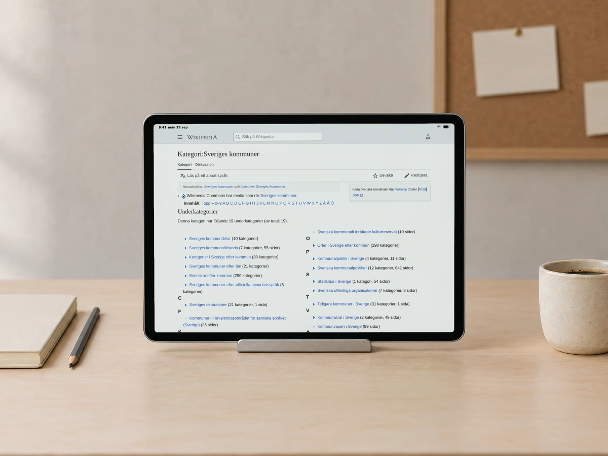 A Wikipedia category page for Sweden's municipalities, with its subcategories and page counts, on a tablet in a stand on a birch desk in a design studio